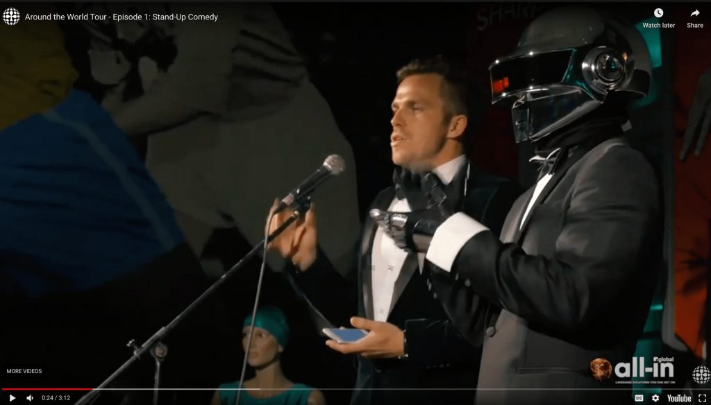 Around the world tour video screen shot with Roy dressed as Daft Punk next to host