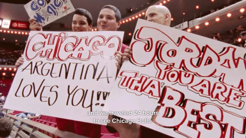 Chicago Bulls supporters in the stands of a game in the nineties holding boards and explaining they's traveled 24h to watch the game